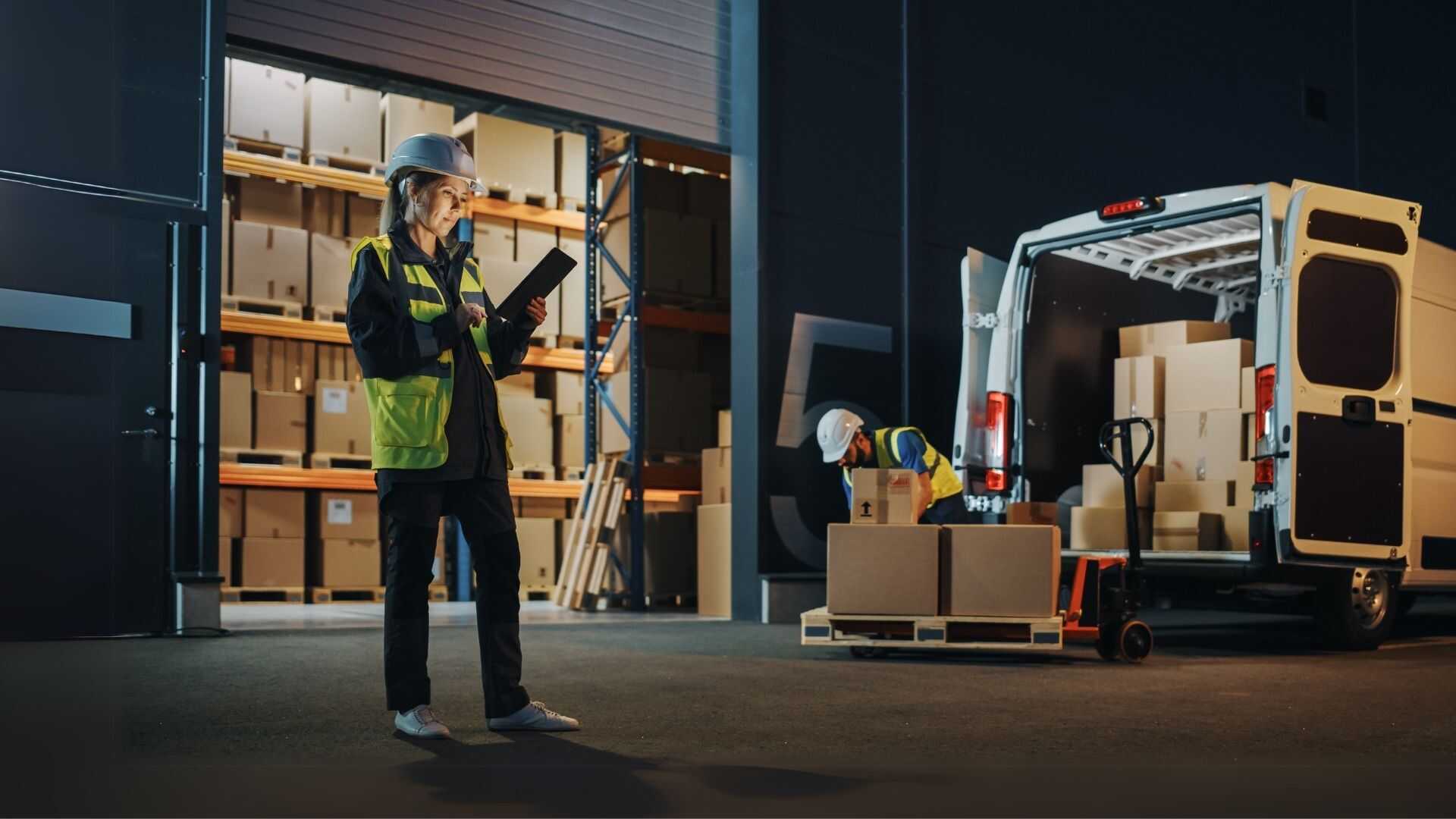 Last-mile logistics manager standing in front of a warehouse and loaded cargo truck ensuring coordinated charter freight delivery.